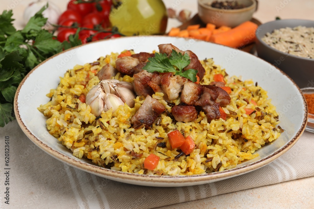 Delicious pilaf with meat, carrot and garlic on beige table, closeup