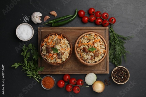 Delicious pilaf in bowls and products on black table, flat lay
