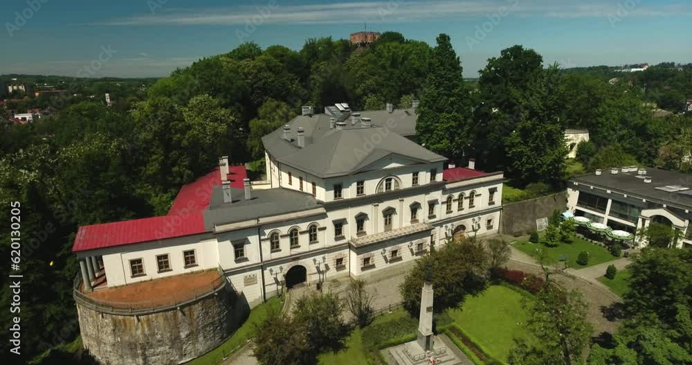 A historic and restored manor house on a hill, surrounded by a park with green trees during summer in Poland, captured in a dynamic 4K drone shot. A historic and restored manor house on a hill, surrounded by a park with green trees during summer in Poland, captured in a dynamic 4K drone shot.