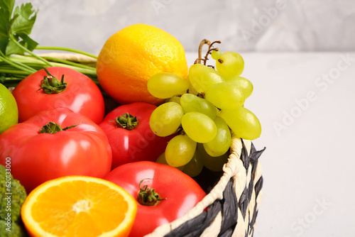 Wicker bowl with different fresh fruits and vegetables on white table  closeup