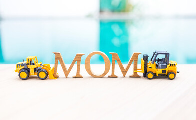 Mom wooden font with two toy truck on swimming pool edge with space on blurred water background, mother's day card background idea, industry style