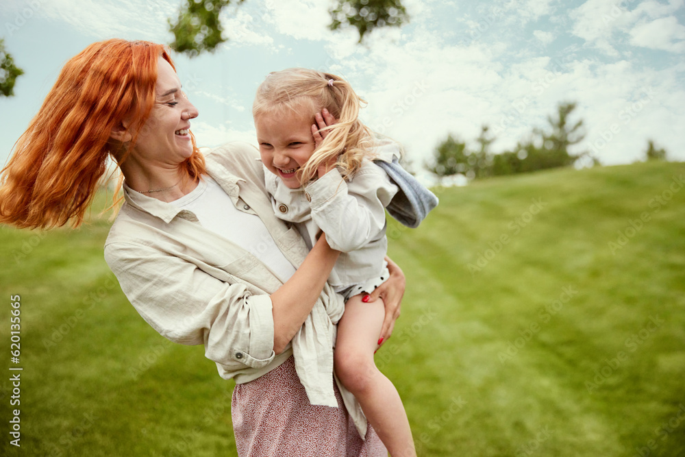 Happiness. Beautiful redhead young woman, mother playing with her little daughter in the park on warm summer day. Concept of family, childhood and parenthood, fun, weekends, love, ad Happiness. Beautiful redhead young woman, mother playing with her little daughter in the park on warm summer day. Concept of family, childhood and parenthood, fun, weekends, love, ad