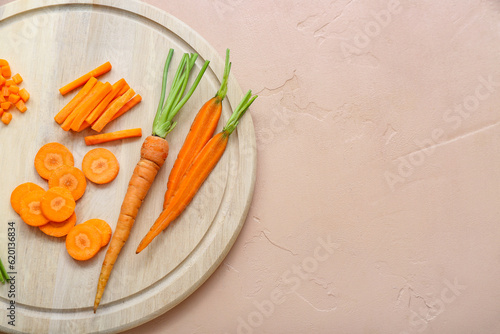Wooden board with fresh carrot and slices on beige background