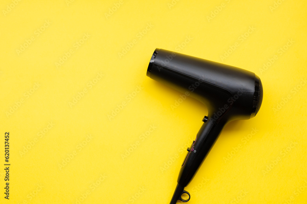 Fototapeta premium Black hair dryer on blue and yellow paper background
