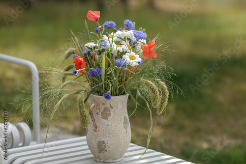 Wild flower bouquet (Cornflowers, chamomiles wheat and poppies) in terracotta vase. Wildflower and grass varieties.