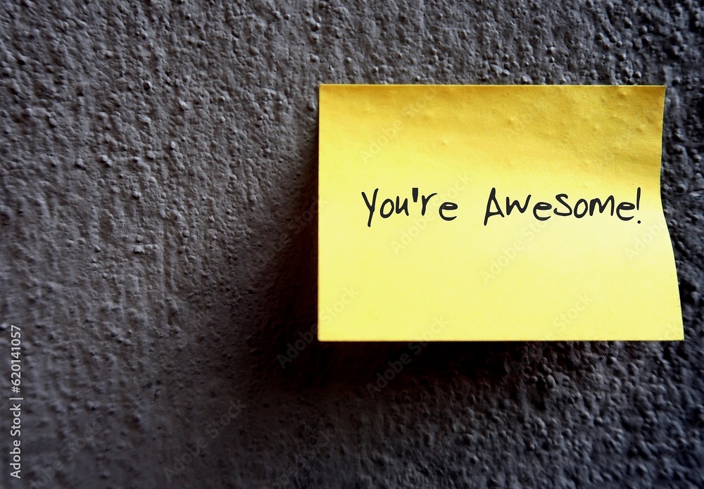 Yellow note on copy space wall background with text written YOU'RE ...