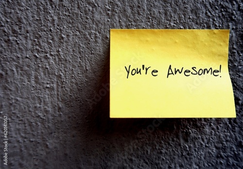 Yellow note on copy space wall background with text written YOU'RE AWESOME!, to Fototapeta