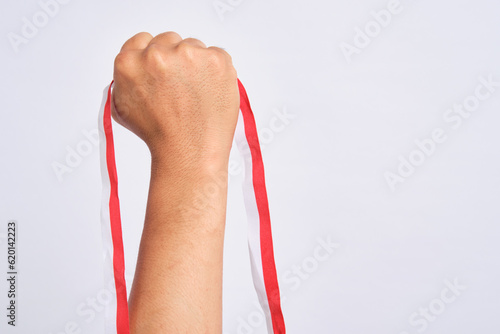 Human hand holding a red and white ribbon as a symbol of the Indonesian flag isolated on gray background photo