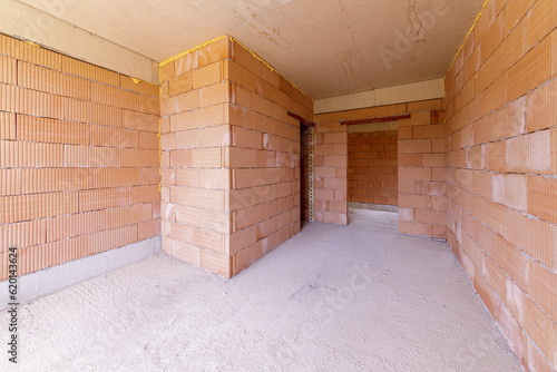 Unfinished room interior of building under construction. Brick red walls. New home. © dechevm