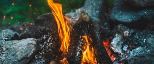 Vivid smoldered firewoods burned in fire close-up. Atmospheric background with orange flame of campfire. Full frame image of bonfire. Warm whirlwind of glowing embers and ashes in air. Sparks in bokeh © Daniil