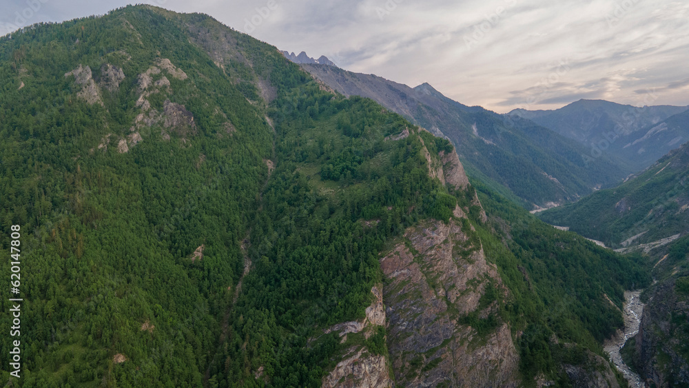 Fototapeta premium Aerial view of a high valley of the rocky mountain range, on which snow lies in places, near to the fast mountain river at summer cloud morning, yellow color