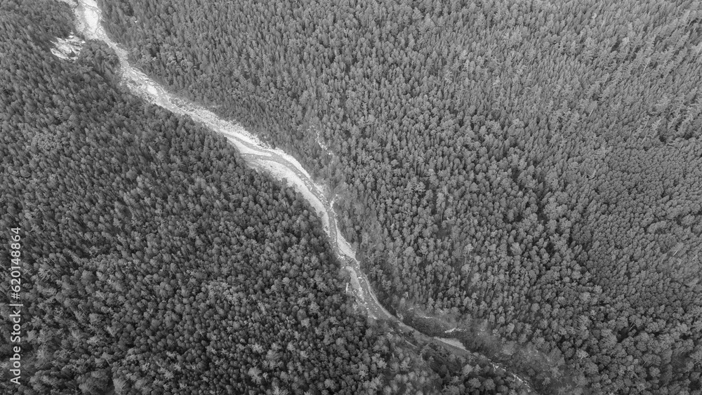 Obraz premium Aerial view of the high waterfall and fast mountain river in valley of the rocky mountain ranges, on which snow lies in places at summer cloud morning, gray