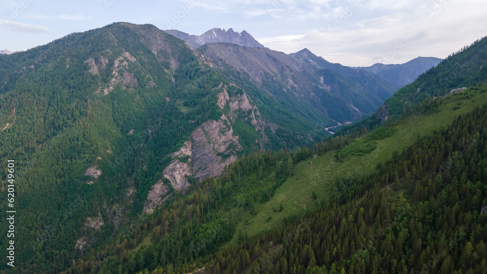 Aerial view of a high valley of the rocky mountain range, on which snow lies in places, near to the fast mountain river at summer cloud morning, orange color of the photo