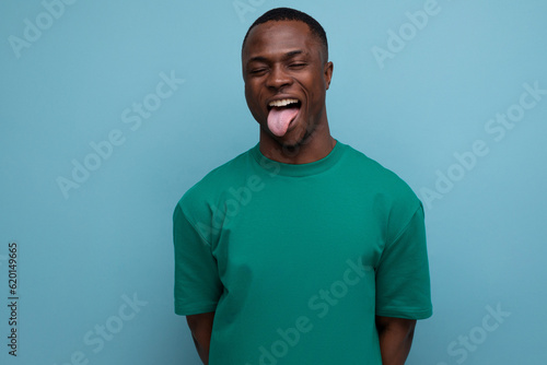 funny young american man in t-shirt makes a grimace on a blue background with copy space