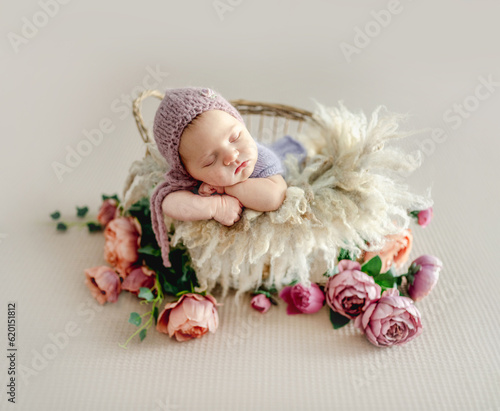 Newborn baby girl sleeping on fur and peony flowers. Cute infant child kid napping in basket studio portrait