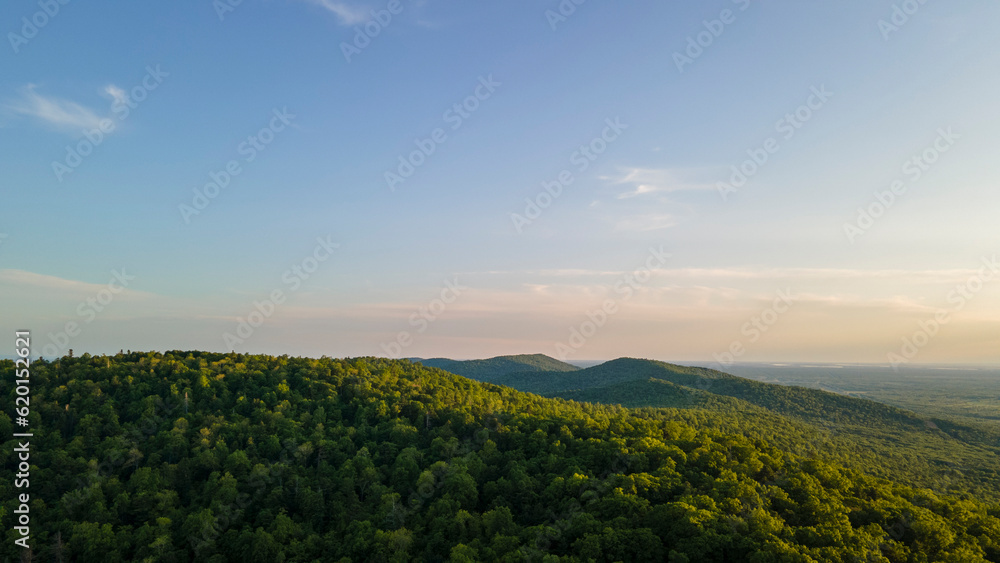 Aerial view of the Peak of the mountain range and tall forest near to the river at summer cloud evening with horizon, yellow color, low height