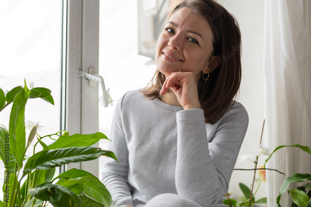 closeup portrait smilling woman sitting near house plants, flowers on window. happy female in cozy green home closeup portrait smilling woman sitting near house plants, flowers on window. happy female in cozy green home