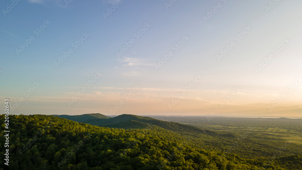 Aerial view of the Peak of the mountain range and tall forest near to the river at summer cloud evening with horizon, shadows, low height