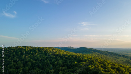 Aerial view of the Peak of the mountain range and tall forest near to the river at summer cloud evening with horizon, low height, blue