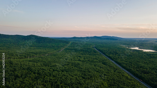 Aerial view of the Mountain range and tall forest near to the river at summer cloud evening with incredible horizon, orange color