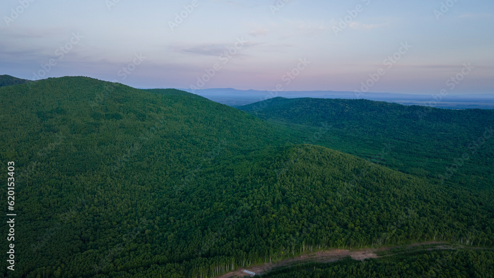 Aerial view of the country road and power lines near to the mountain range, coniferous high forest and the river at summer cloud evening with yellow horizon, color Aerial view of the country road and power lines near to the mountain range, coniferous high forest and the river at summer cloud evening with yellow horizon, color