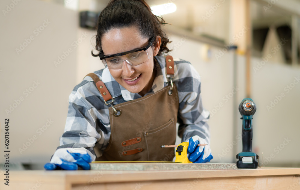 Beautiful Latin woman carpenter using power tools working her wood job in carpenter's shop. Young hispanic female in protective goggles busy in furniture woodworking. Feminism in carpentry industry. Beautiful Latin woman carpenter using power tools working her wood job in carpenter's shop. Young hispanic female in protective goggles busy in furniture woodworking. Feminism in carpentry industry.