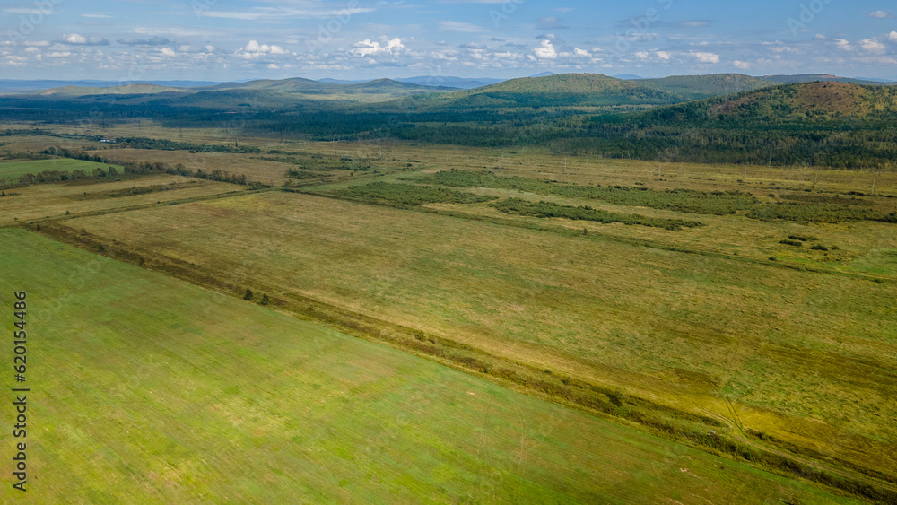 Aerial view of the country road and power lines near to the hill range, small coniferous forest and meadows agriculture at summer cloud sunny with horizon, yellow color Aerial view of the country road and power lines near to the hill range, small coniferous forest and meadows agriculture at summer cloud sunny with horizon, yellow color