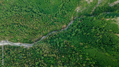 Aerial view of the mountain river in the valley of the rocky mountain ridges, on which snow lies in places at summer cloud morning, orange color of the image, down