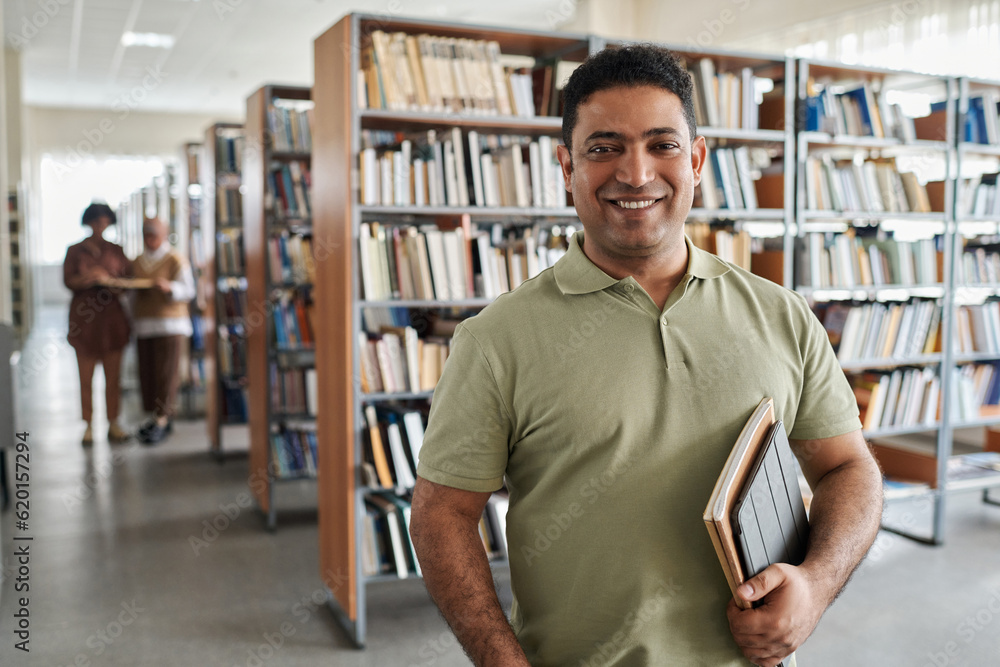 Portrait of adult student smiling at camera while standing in the library - obrazy, fototapety, plakaty 