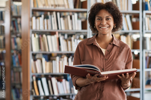 Portrait of African American student smiling at camera while reading book in library photo