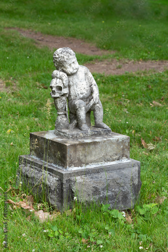 Obraz premium 19th Century statue representing a young baby leaning on a human skull in cemetery