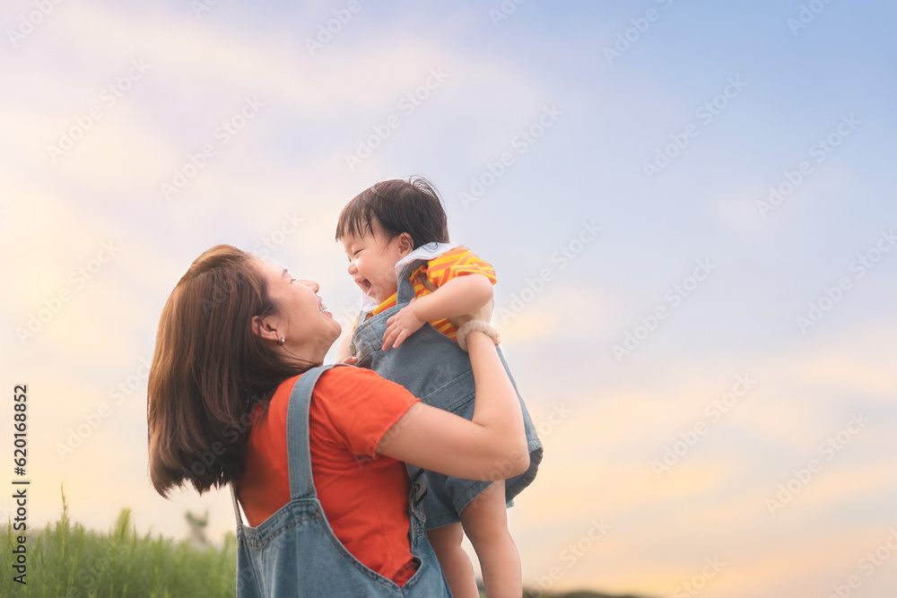 Happy Asian mother plays with daughter and holding girl in hands at park with nice sky, Baby smile and laughing, Family concept. Happy Asian mother plays with daughter and holding girl in hands at park with nice sky, Baby smile and laughing, Family concept.