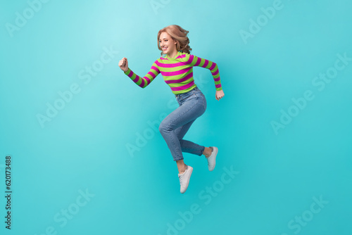 Full length photo of charming purposeful lady wear striped pullover jumping high running fast isolated teal color background