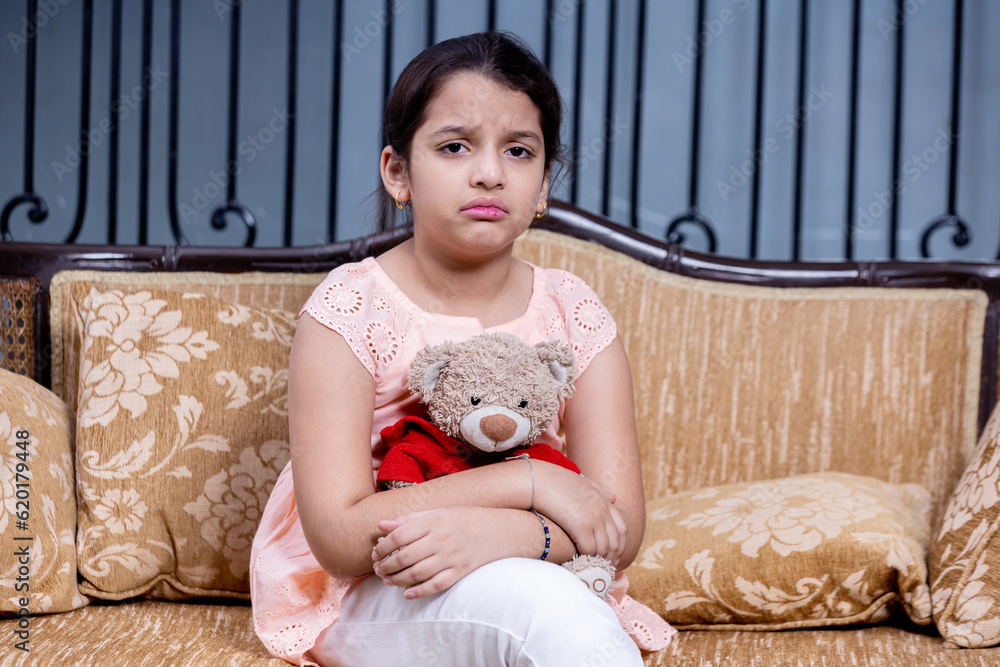 Portrait of indian sad kid sitting on couch holding teddy bear in hand, Kid mental health issue Portrait of indian sad kid sitting on couch holding teddy bear in hand, Kid mental health issue