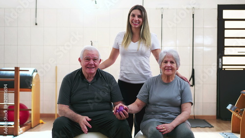 Senior man and woman sitting on Pilates Balls posing for camera with a young Sport Coach inside physiotherapist studio