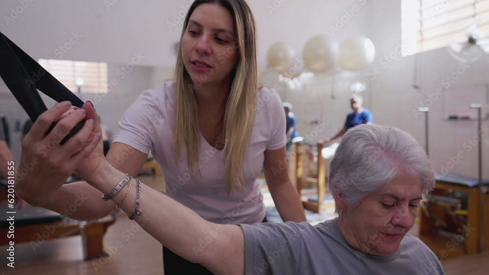 Obraz premium Senior woman exercising in Pilates session with the help of Female Coach instructor, spine health workout routine at old age lifestyle