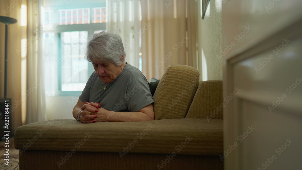 Hopeful senior woman PRAYING at home in solitude. Faithful older female caucasian person with hands clenched having FAITH