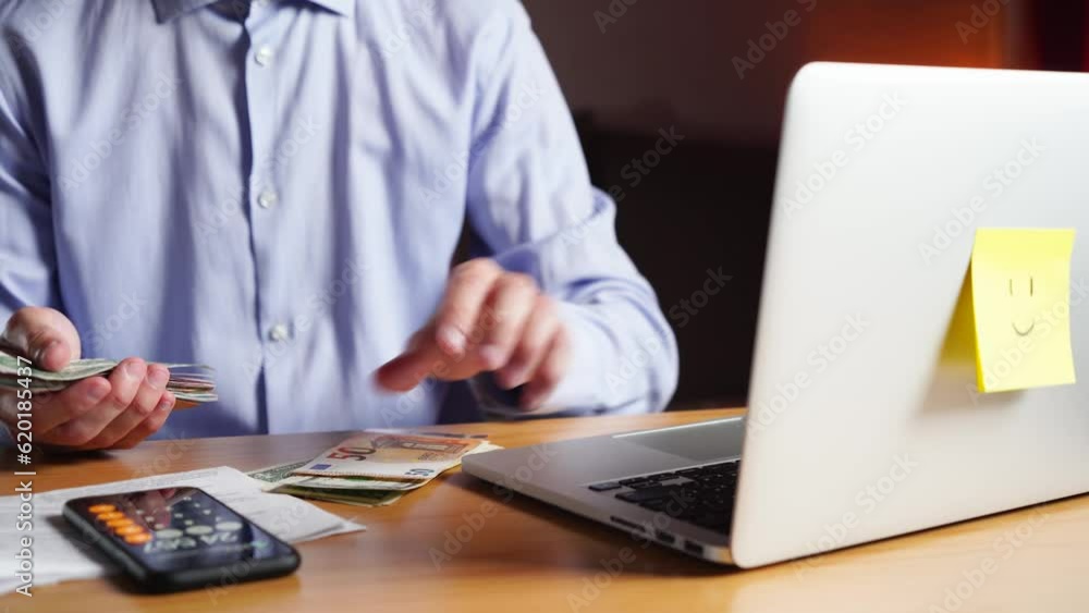 young man in a shirt counting money on a calculator in his home. Workplace. young man in a shirt counting money on a calculator in his home. Workplace.