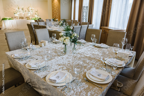 Served banquet tables ready for guests, table with plate, glasses, forks, napkins. Table number 5. Stands, sign number five. Luxury reception. Elegant table decorated composition flowers in party area