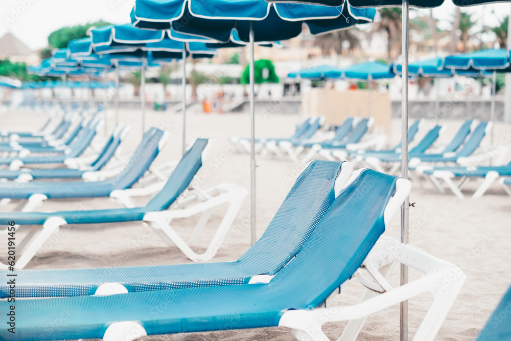 Perspective view on a row of blue empty sunbeds and beach umbrellas in a summer cloudy day Perspective view on a row of blue empty sunbeds and beach umbrellas in a summer cloudy day