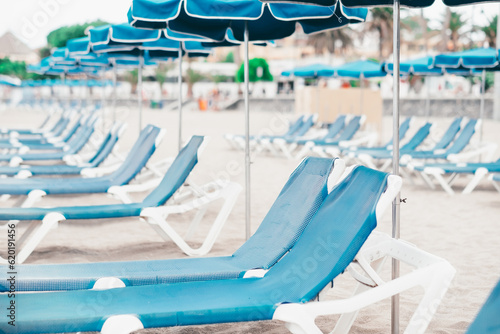 Perspective view on a row of blue empty sunbeds and beach umbrellas in a summer cloudy day