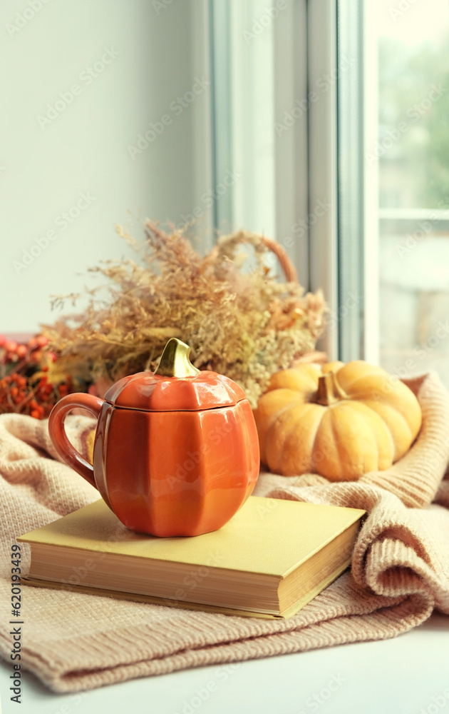 Autumn background. Pumpkin shape cup, book, pumpkin and knitted sweater on windowsill. symbol of fall season. home cozy composition for Halloween, Thanksgiving holiday