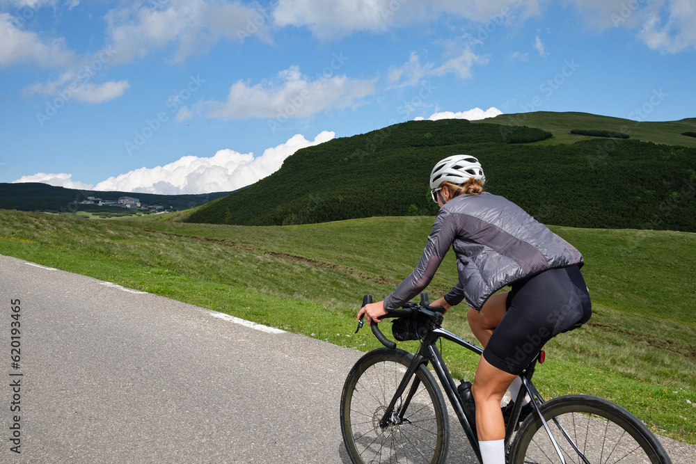 Female cyclist riding a road bike with a view of the mountains.Training for competition.Practicing cycling on open country road. Bucegi Natural Park.