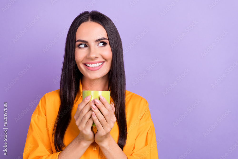 Photo of young dreaming girl wear orange shirt hold cup fresh coffee good flavor look empty space cafe isolated on violet color background Photo of young dreaming girl wear orange shirt hold cup fresh coffee good flavor look empty space cafe isolated on violet color background