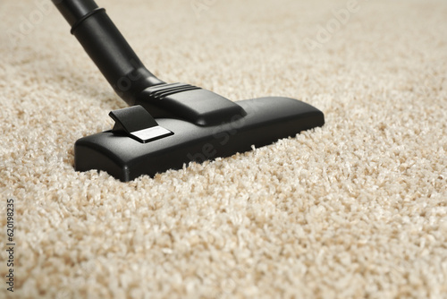 Hoovering beige carpet with modern vacuum cleaner, closeup. Space for text