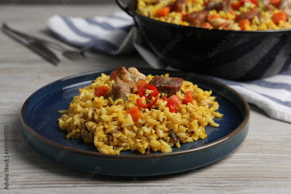 Delicious pilaf with meat, carrot and chili pepper on wooden table, closeup Delicious pilaf with meat, carrot and chili pepper on wooden table, closeup
