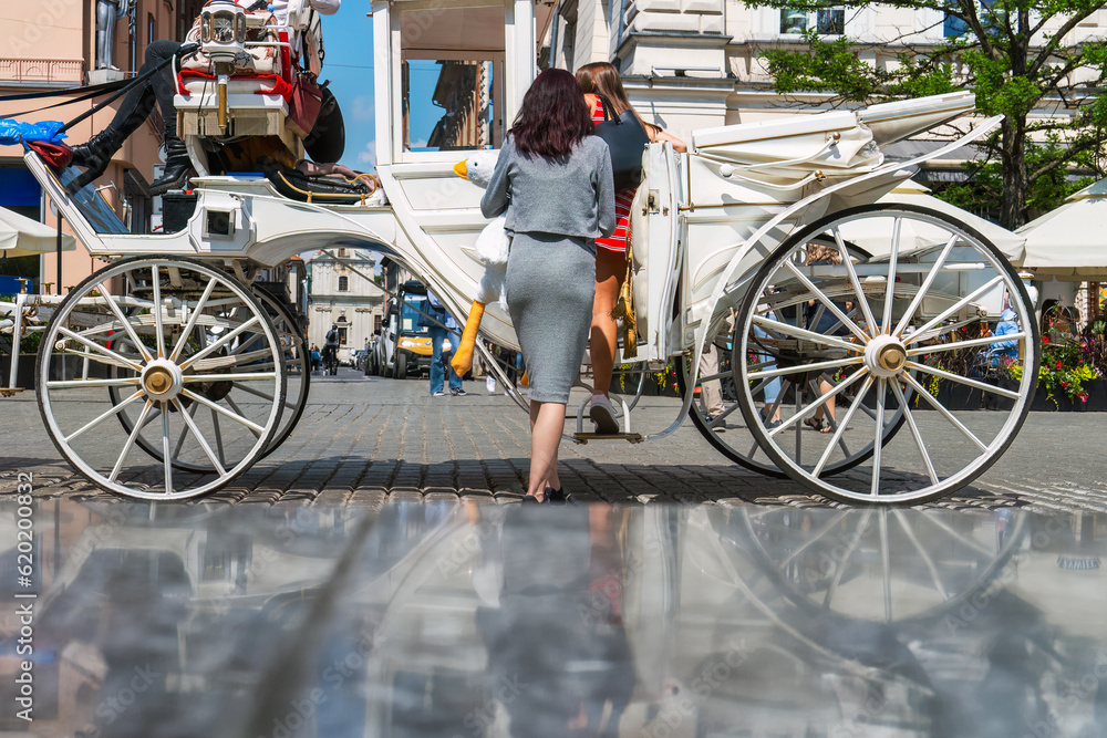 Φωτογραφία Two women get into a white horse-drawn carriage on a sunny day along the cobbled street of an old European city
