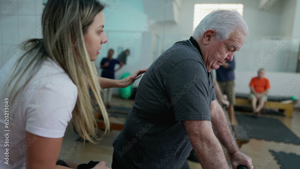 Female Pilates instructor coaching elderly man to exercise with machine inside Physiotherapy studio Female Pilates instructor coaching elderly man to exercise with machine inside Physiotherapy studio