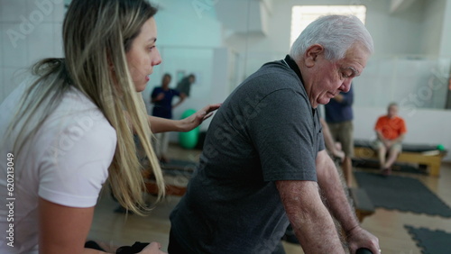 Female Pilates instructor coaching elderly man to exercise with machine inside Physiotherapy studio