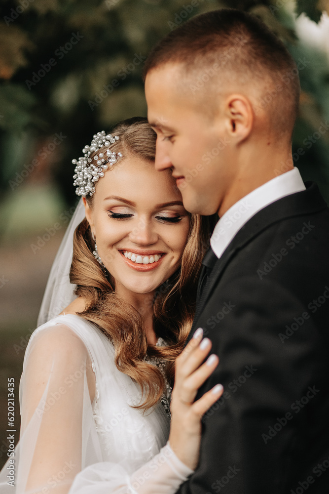 couple in love in the autumn park. Blonde bride in a wedding dress with sleeves. The groom is in a classic black suit, white shirt and tie.